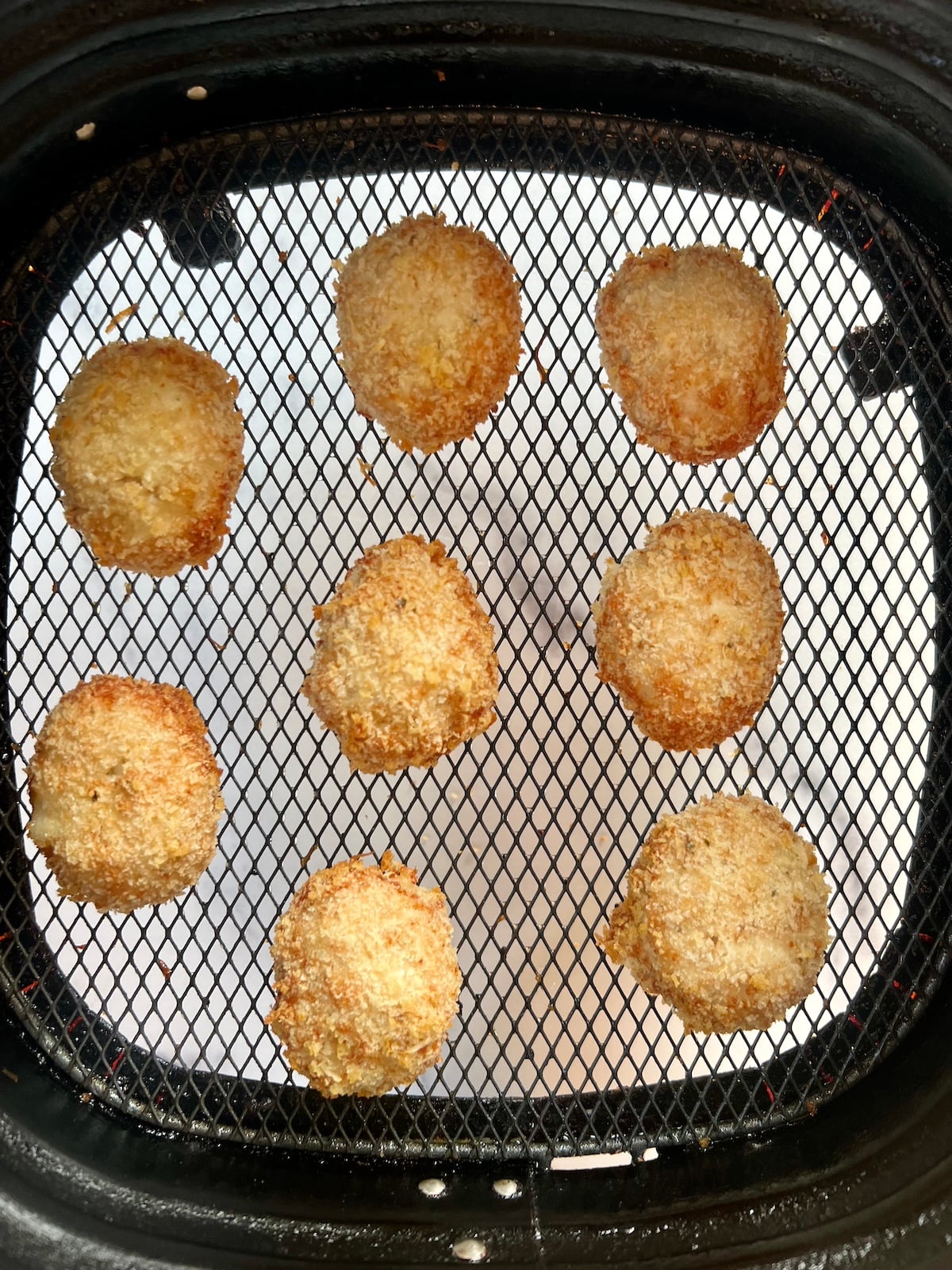 Cooked chicken nuggets in air fryer basket.