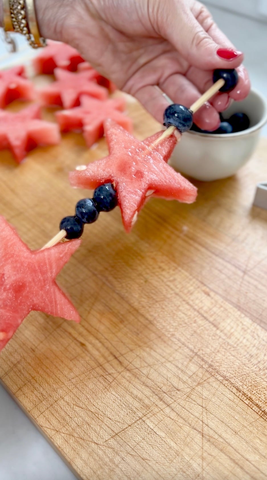 Skewering star shaped watermelon slices and blueberries on bamboo skewer.