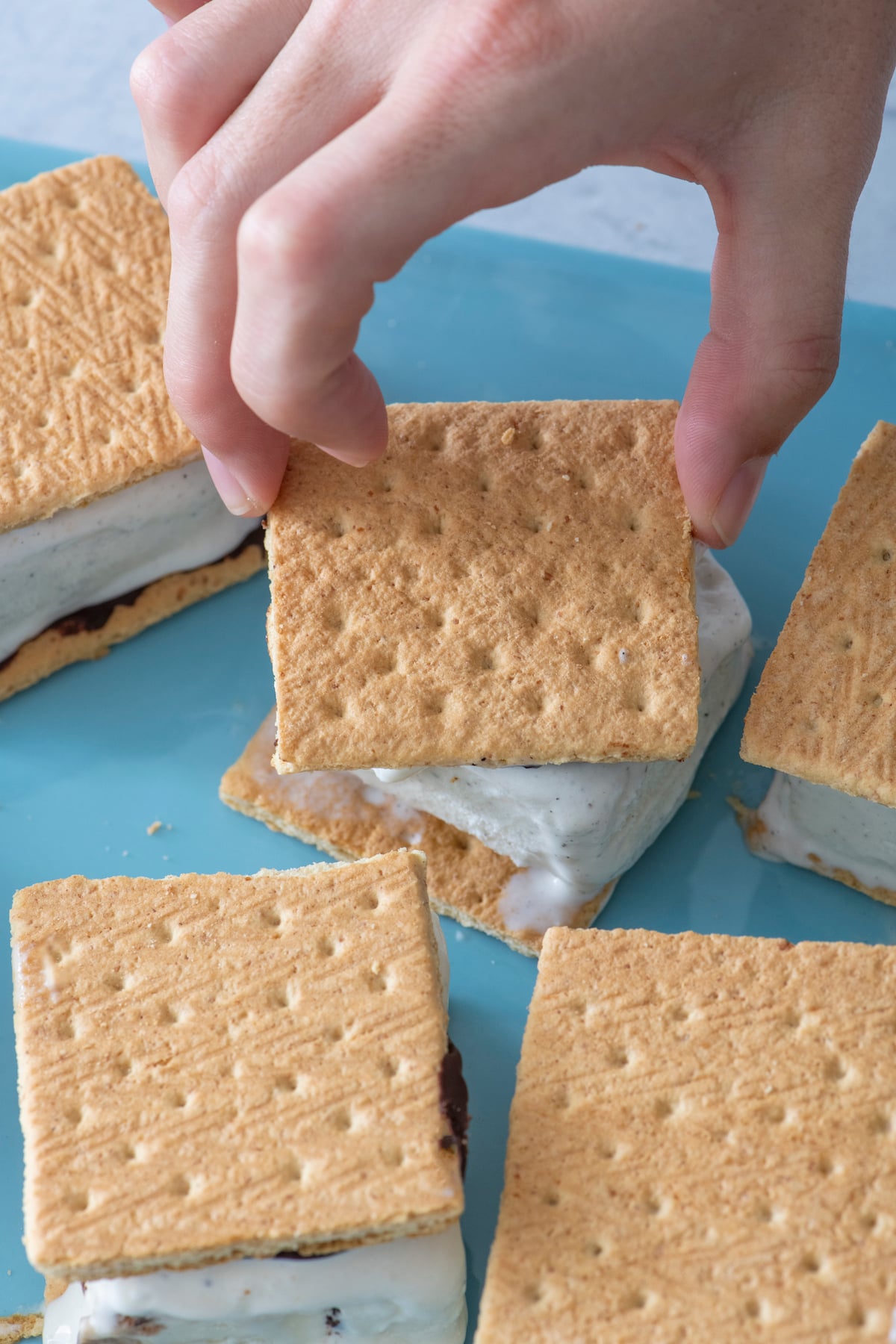 hand placing graham cracker on top of ice cream sandwich