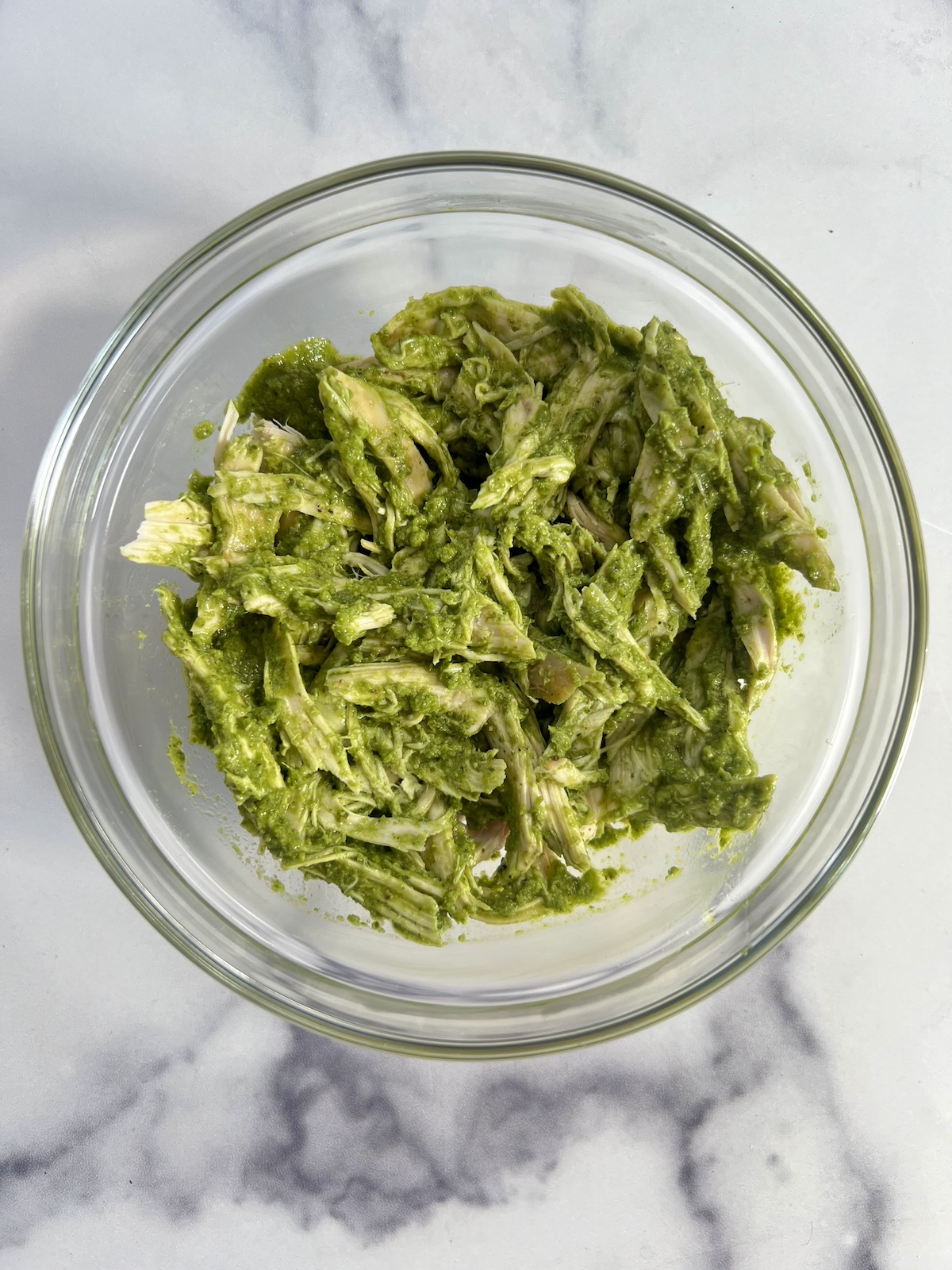 Cooked chicken mixed with pesto in a bowl.