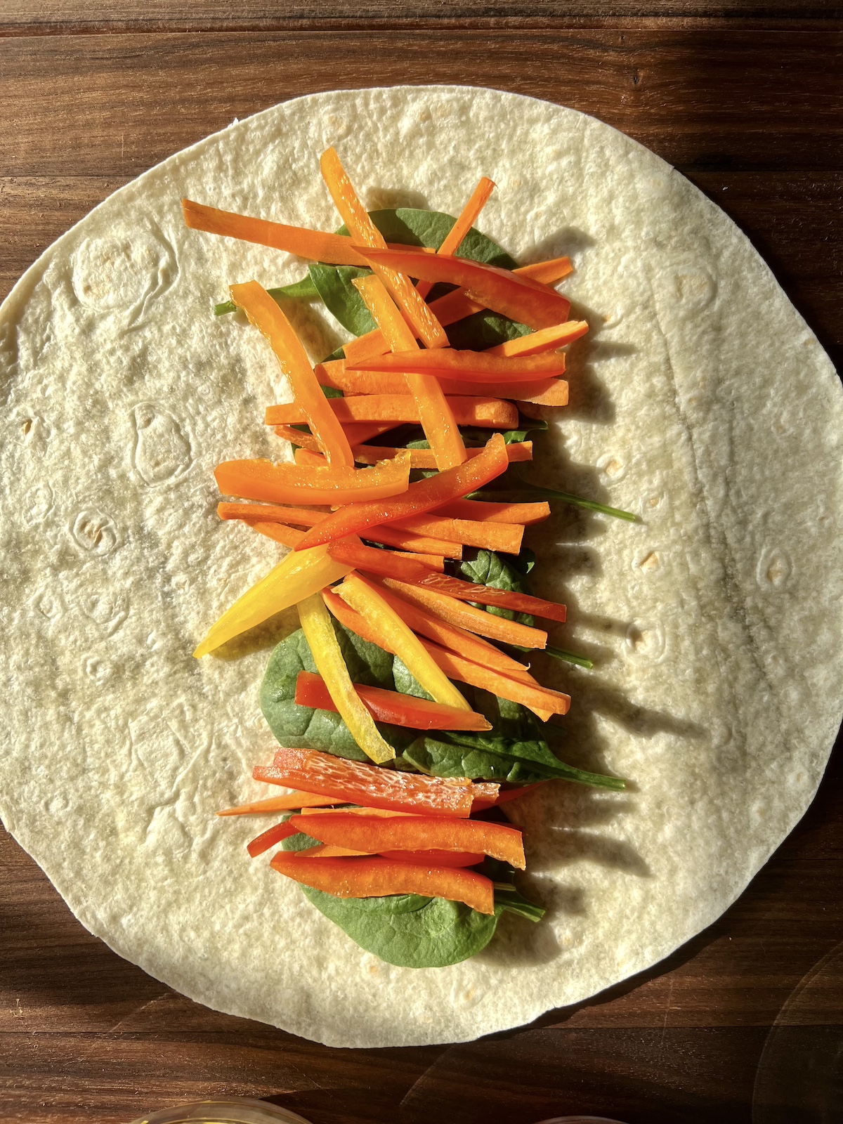 Spinach, sliced carrots and bell peppers on top of a tortilla wrap.