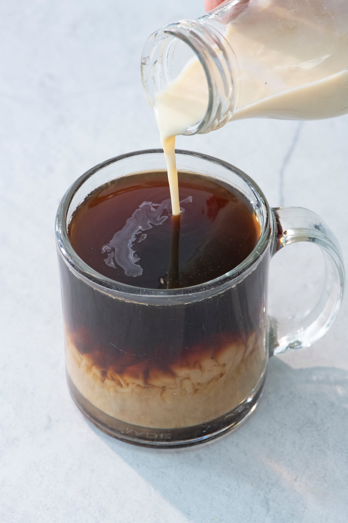 Pouring coffee creamer into cup of coffee.