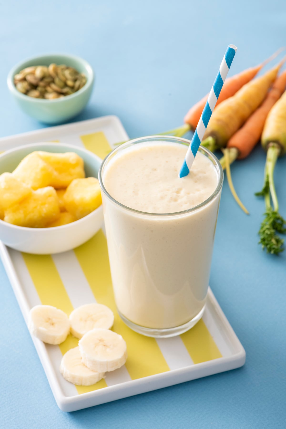 PMS Smoothie in foreground with pineapple, carrots and pumpkin seeds in background.