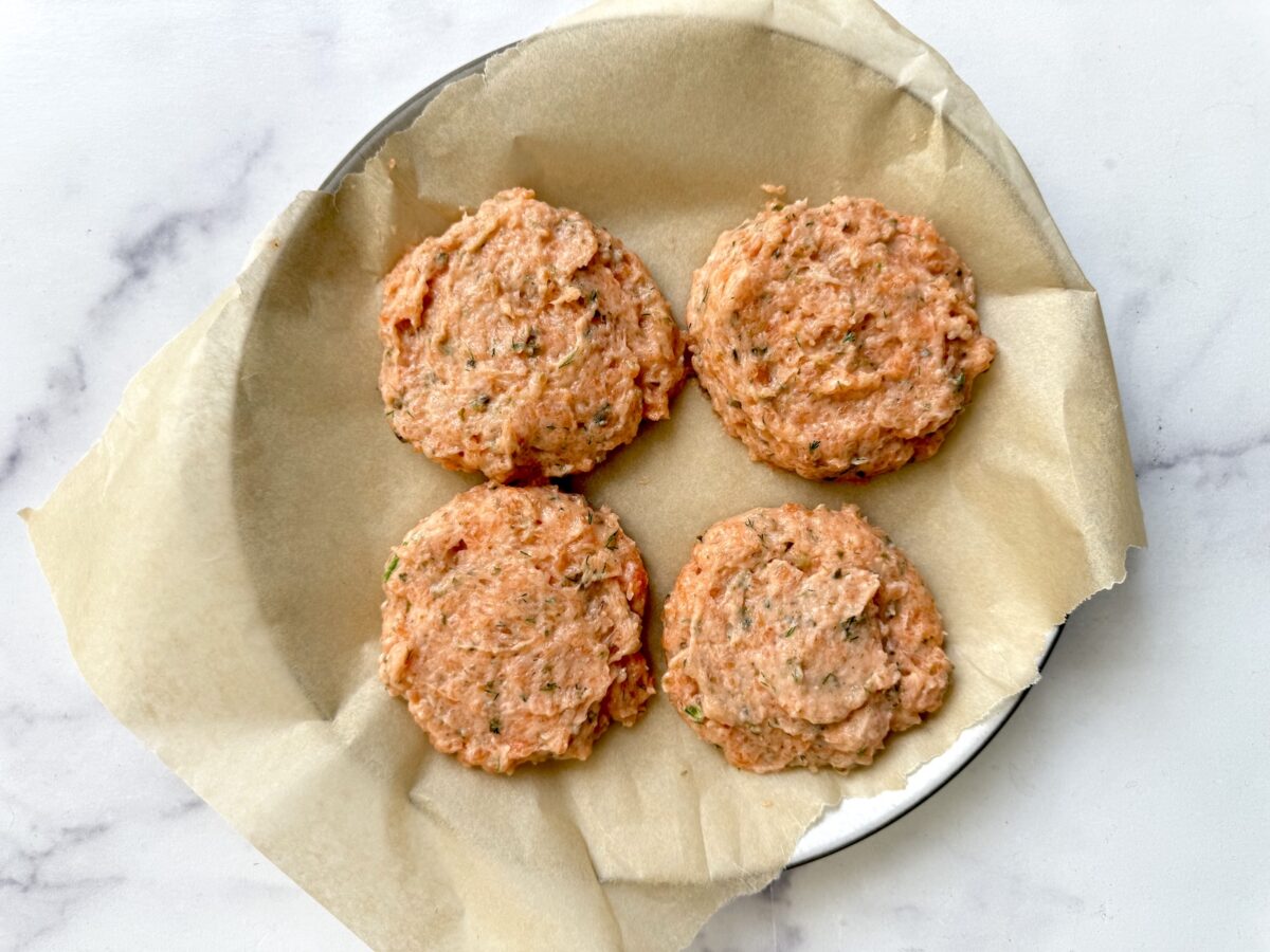 Four salmon burger patties on a parchment line plate.