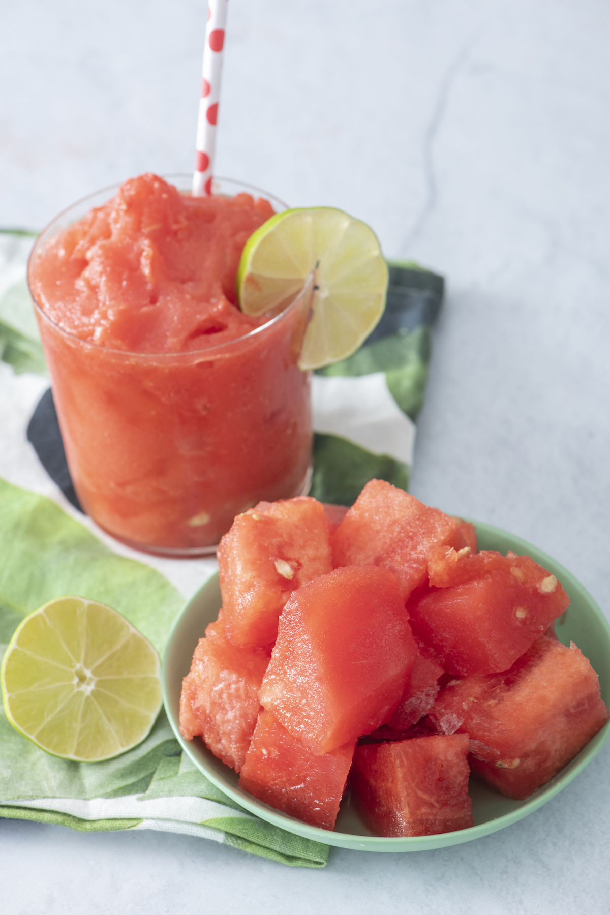 Chunks of watermelon in a bowl in the foreground with a watermelon slushie in the background.