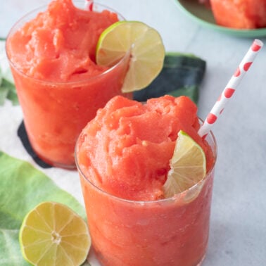 Two watermelon slushies in glasses with lime wedges.