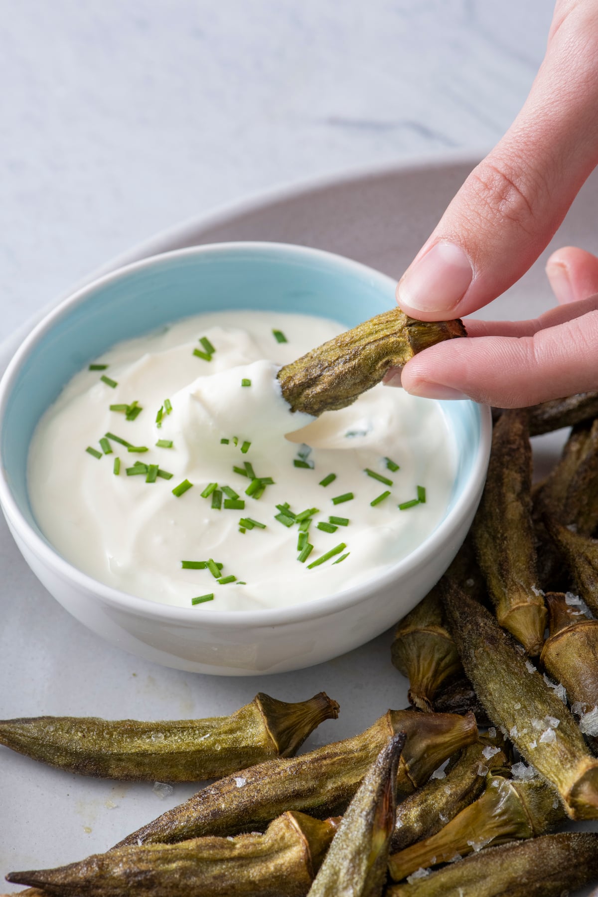 Hand dipping air fried okra in veggie dip.