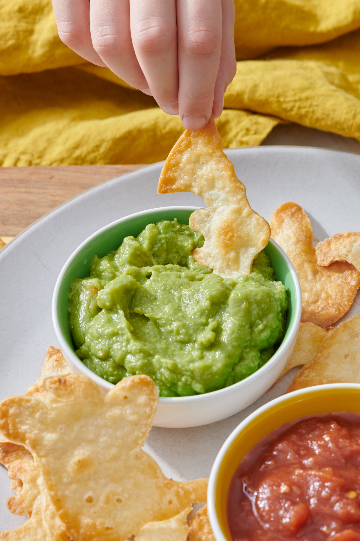 Hand dipping bat shaped tortilla chip into guacamole.