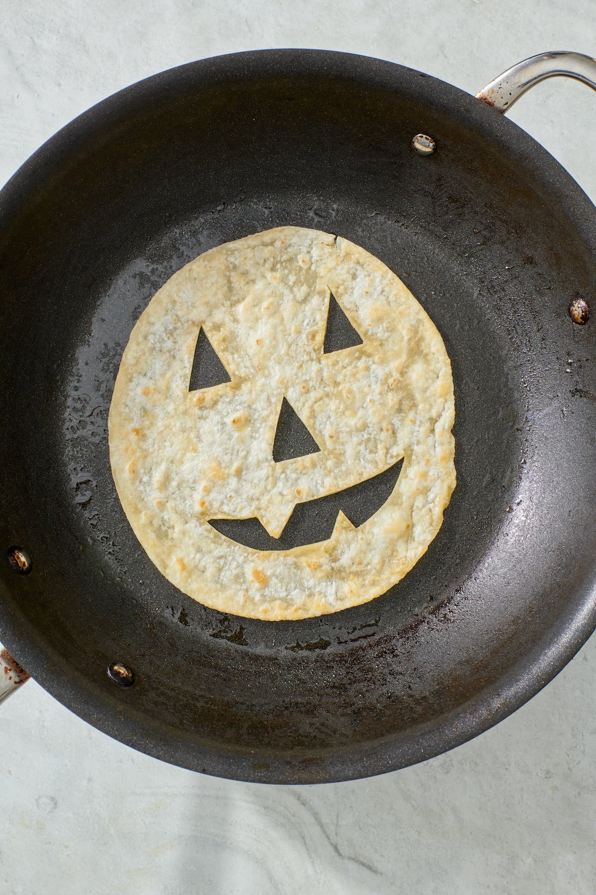 Jack-o'-lantern face tortilla on frying pan.