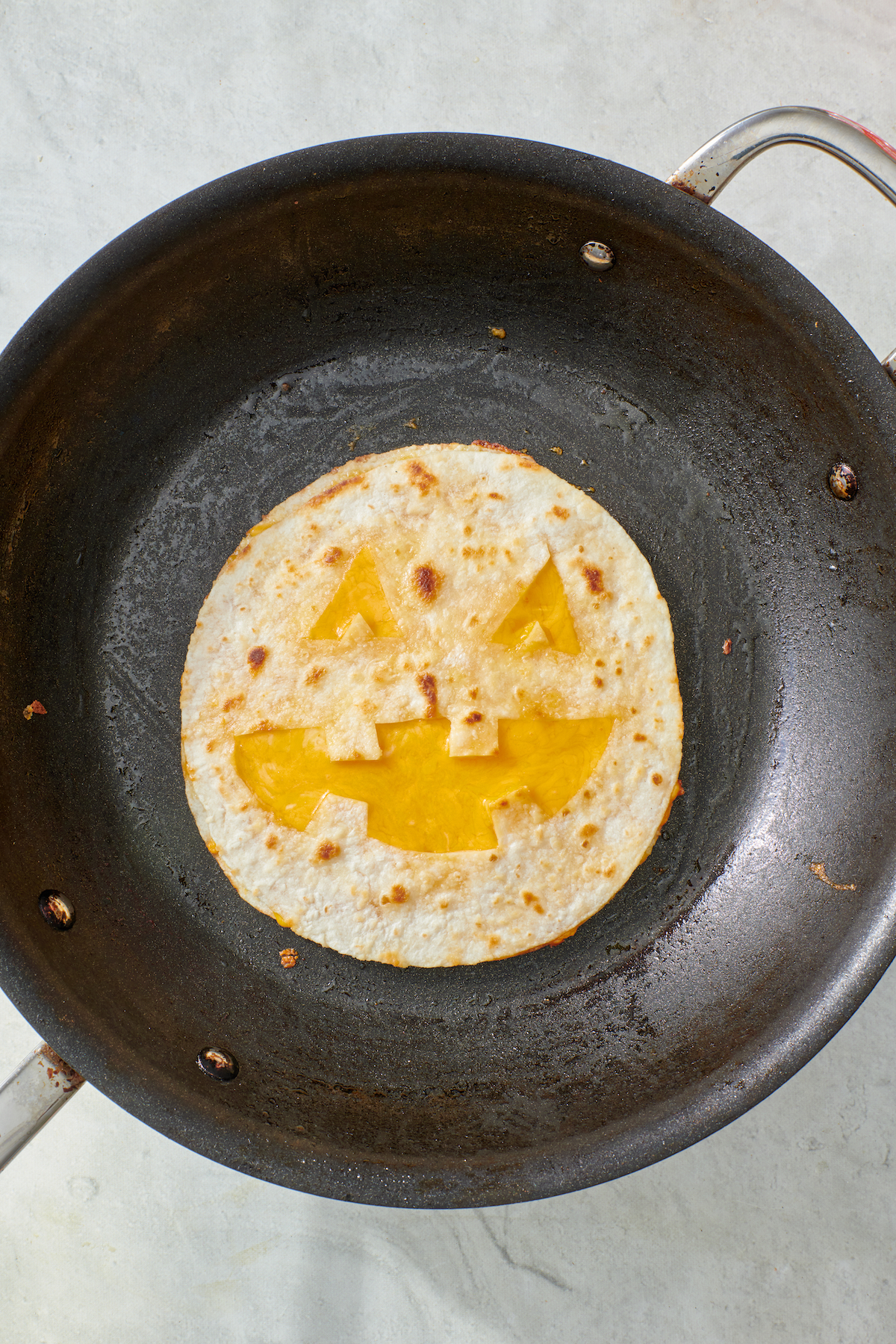 Completed jack-o'-lantern quesadilla on frying pan.