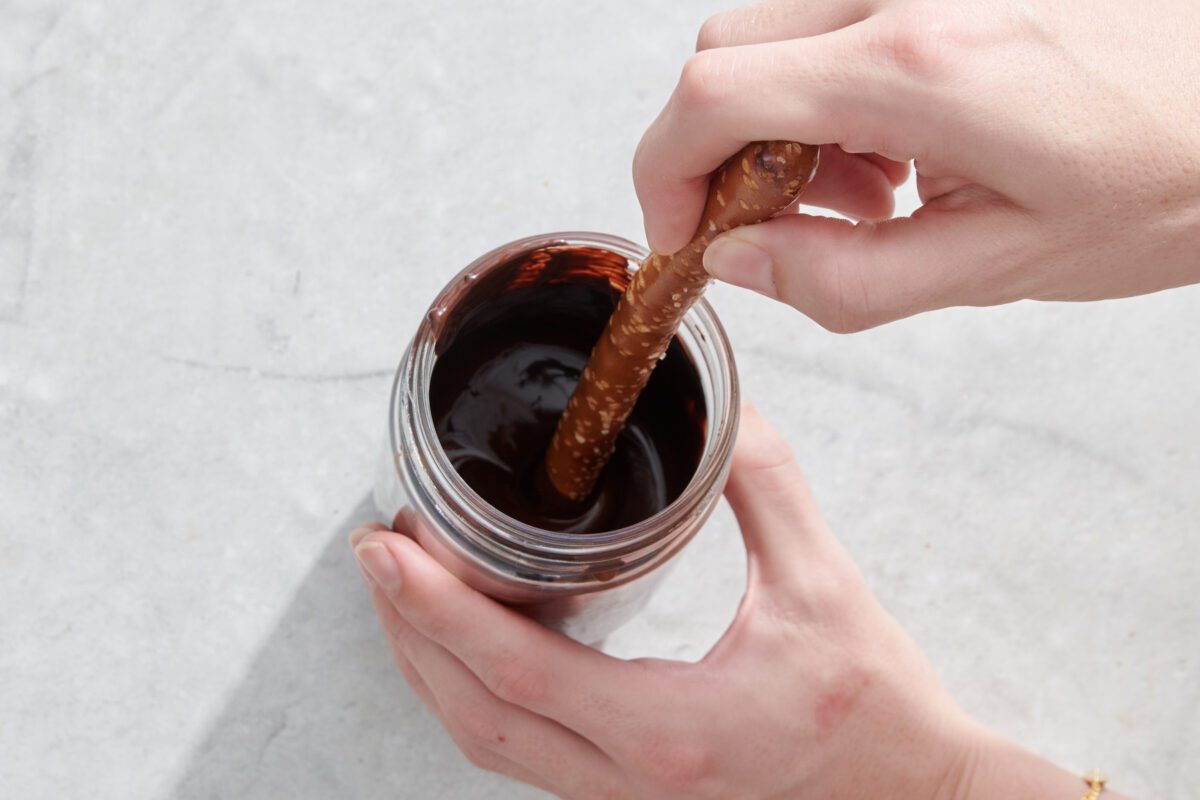 Dipping pretzel rod into melted chocolate.