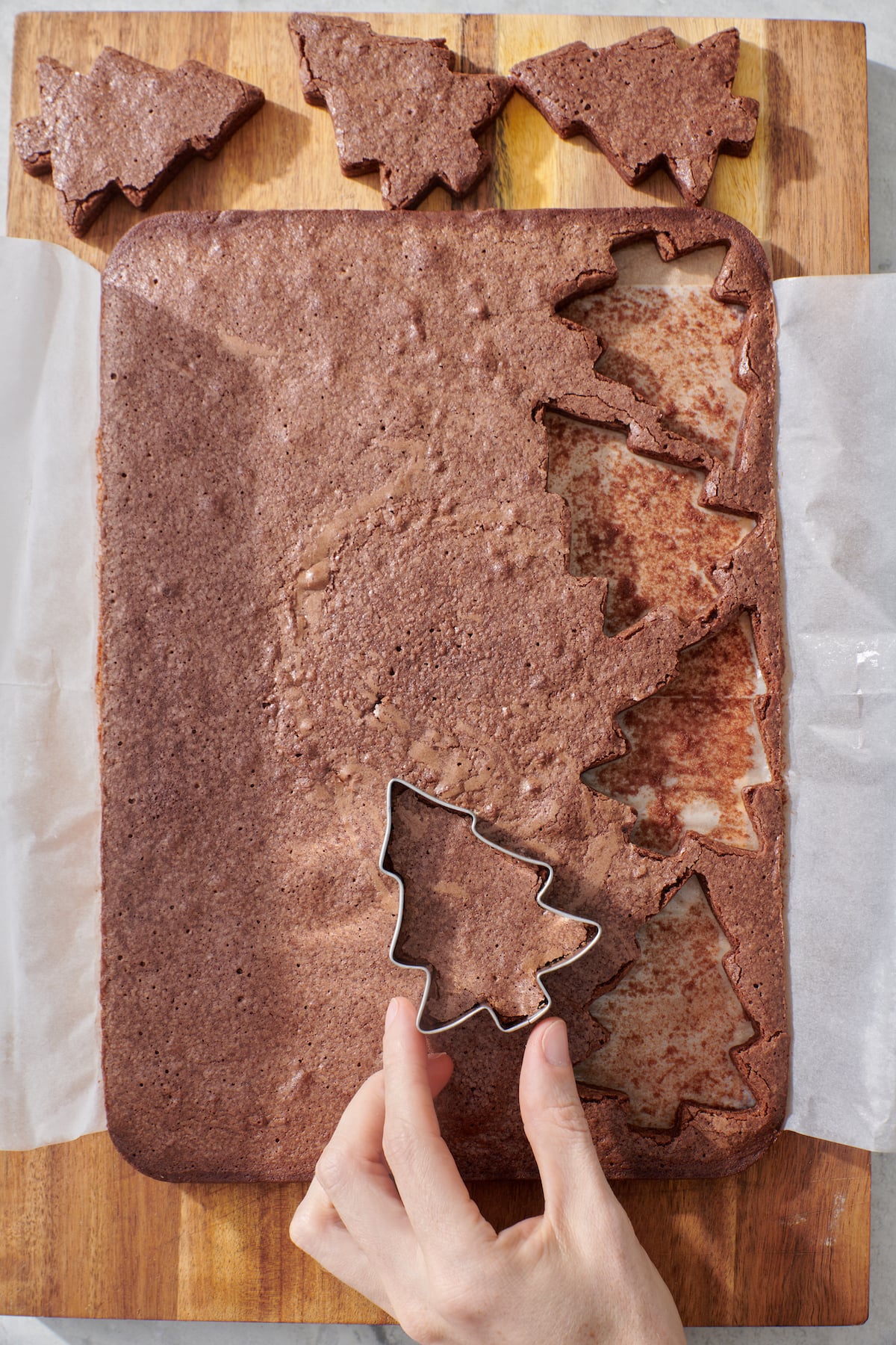 Hand using cookie cutter to cut out holiday tree shapes.