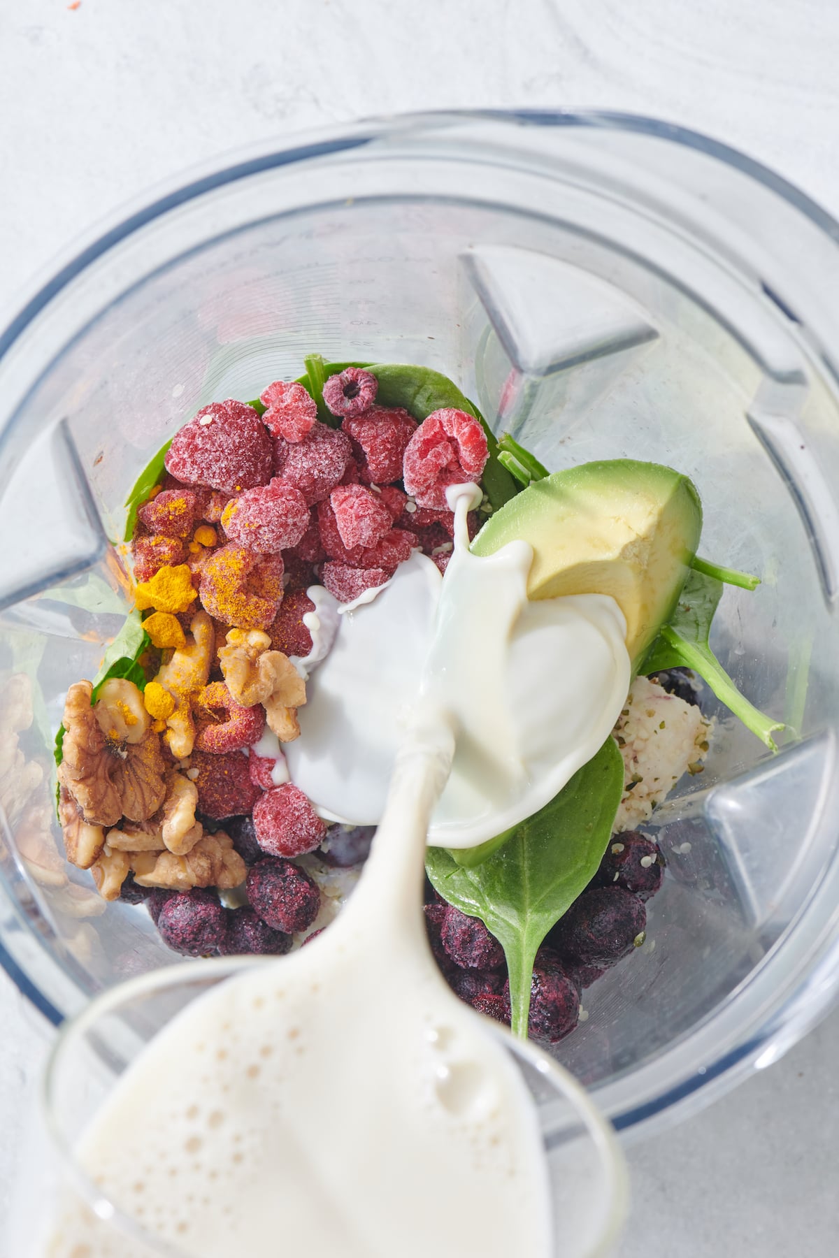 Pouring milk into blender containing brain boosting smoothie ingredients.