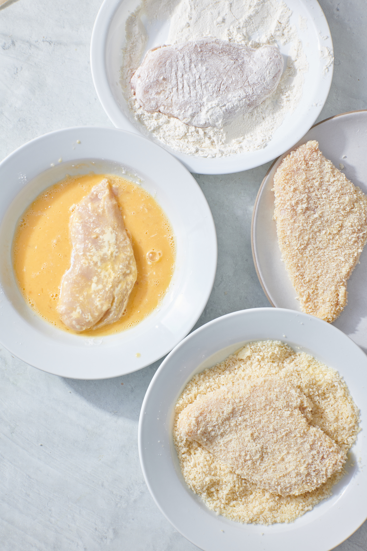 One chicken breast in bowl of flour. One chicken breast in egg wash. One chicken breast in panko mixture.