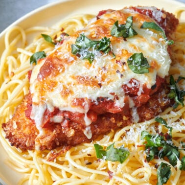 Chicken parmesan atop a bed of spaghetti noodles.