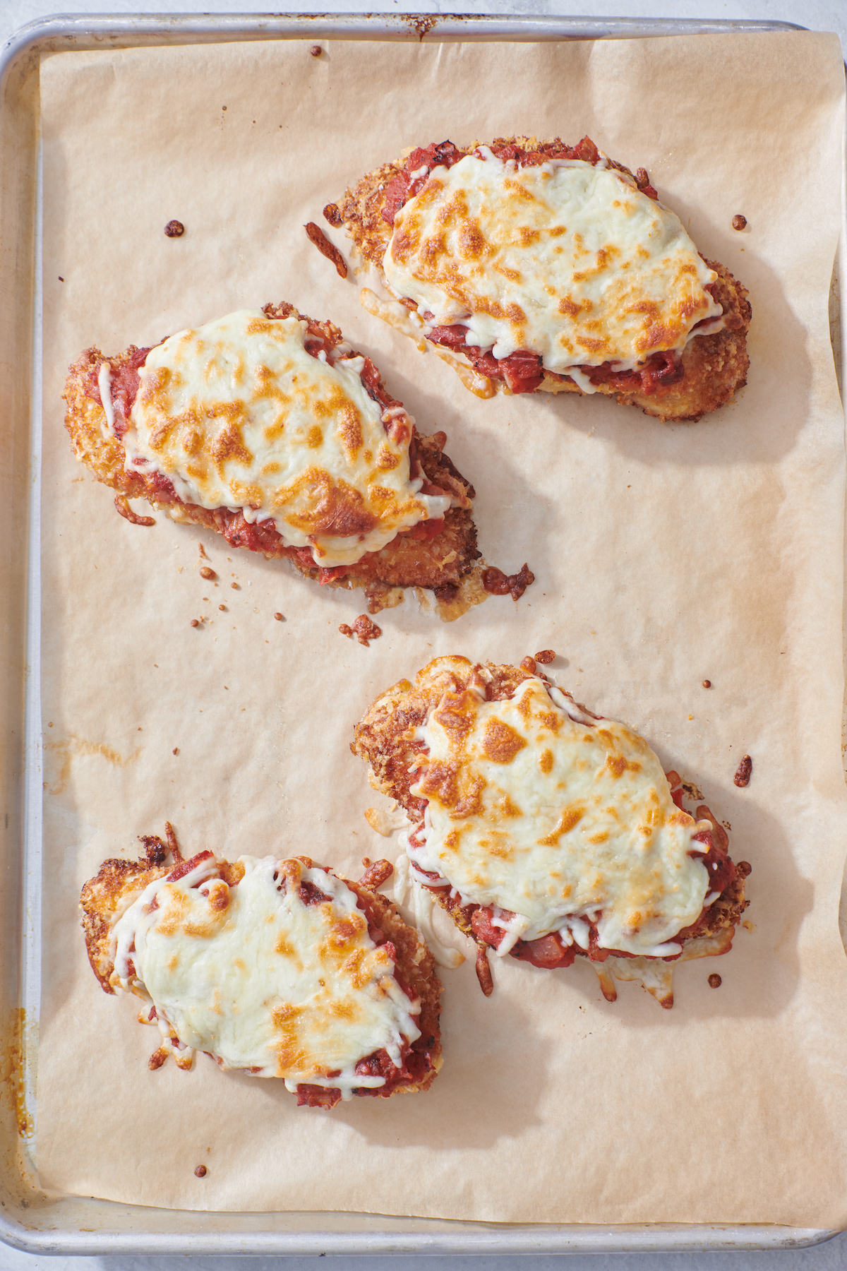 Cooked Crispy Chicken Parmesan on parchment lined baking sheet.