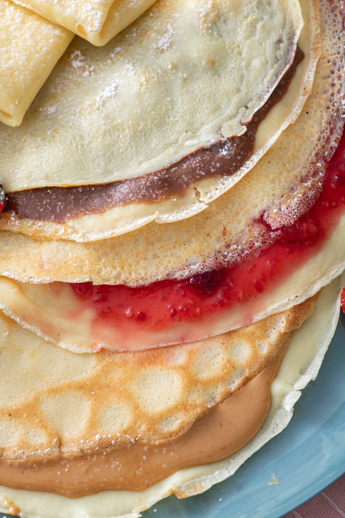 Three crepes. One filled with Nutella, one with fruit preserves and one with peanut butter.