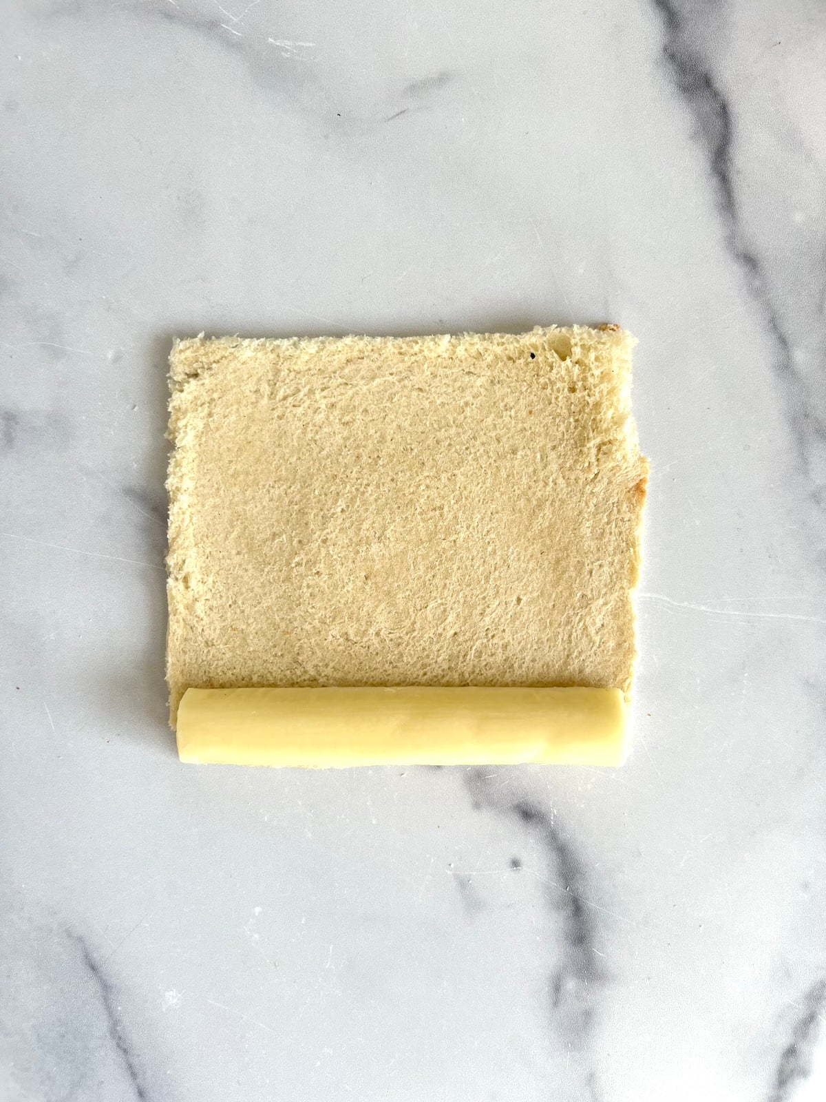 Mozzarella cheese stick ready to be rolled in sandwich bread.