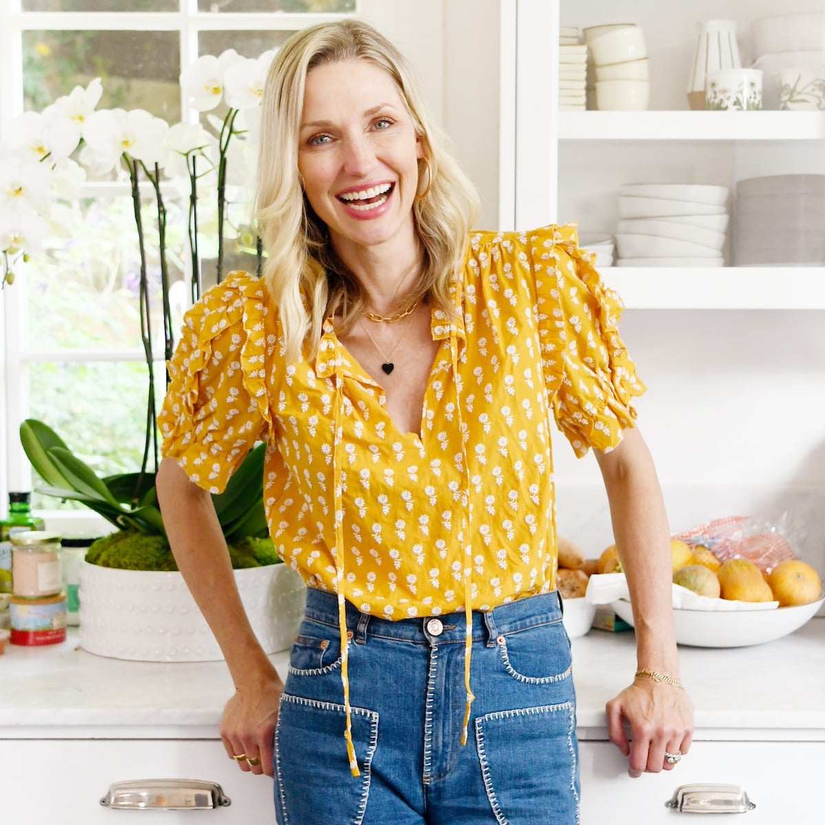 Catherine McCord smiling for camera in the kitchen wearing a yellow shirt.