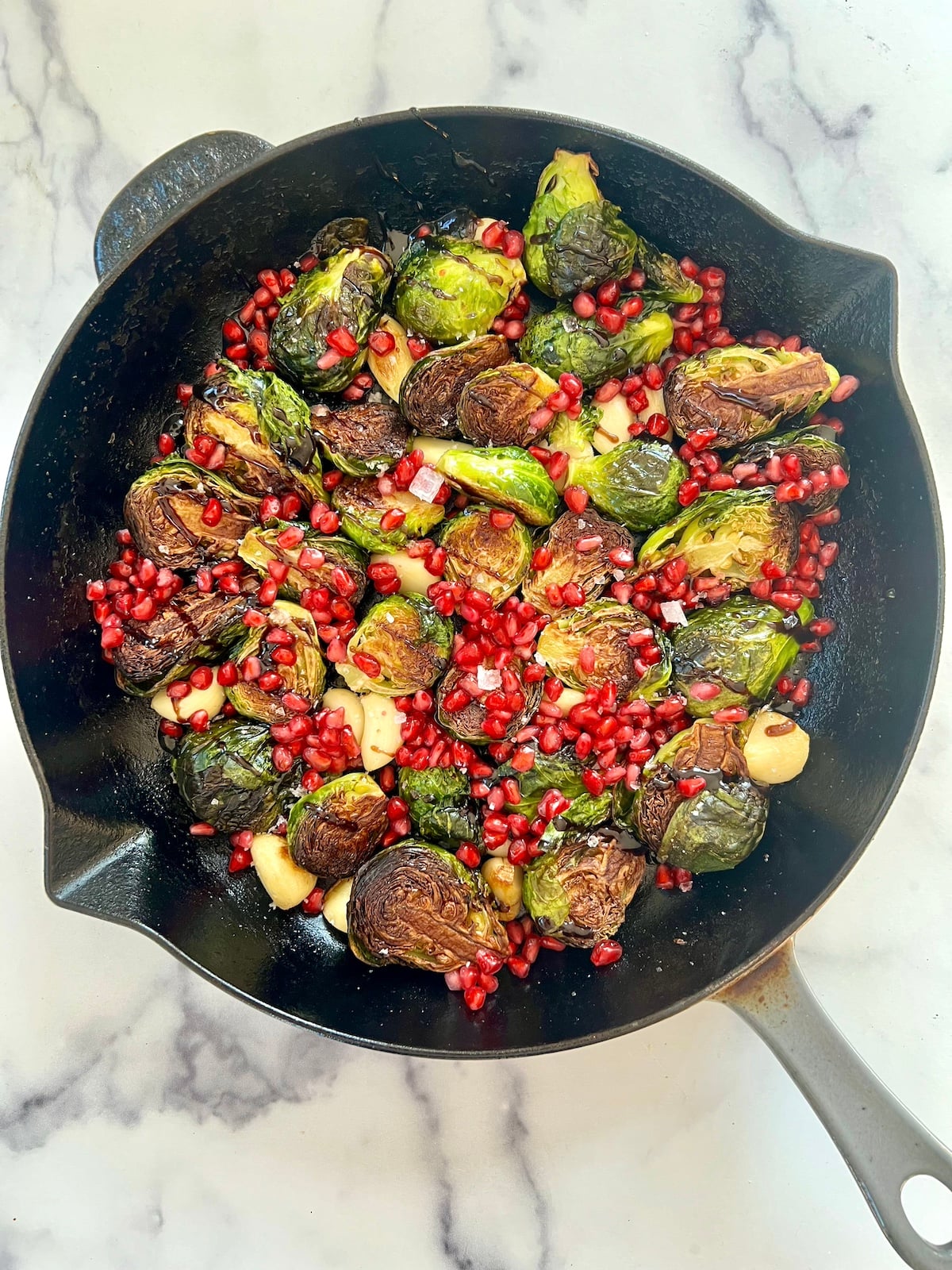 Cast iron Brussels sprouts with garlic, pomegranate seeds and other toppings in skillet.