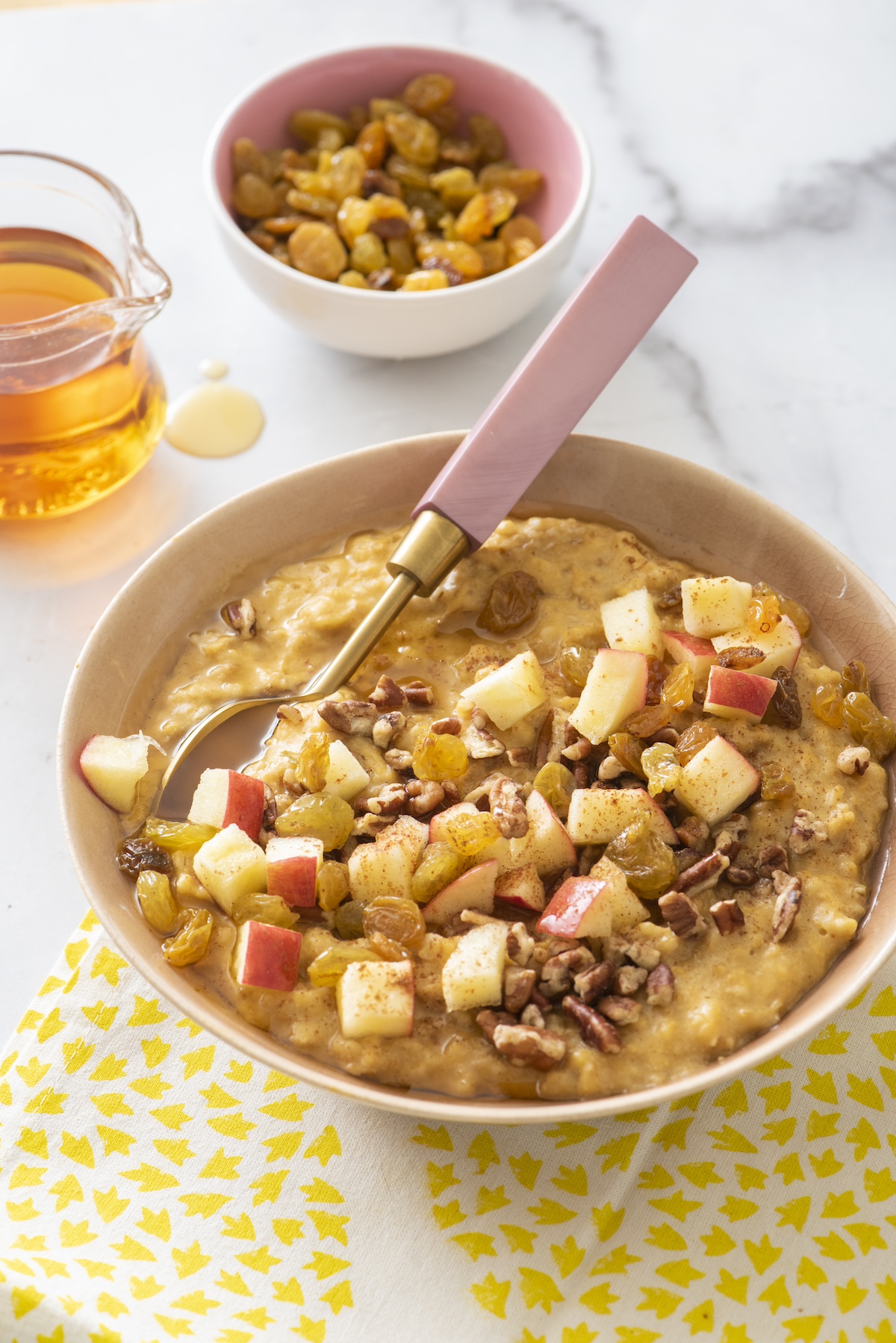 Pumpkin spice oatmeal in a bowl topped with chopped apples, raisins and walnuts.