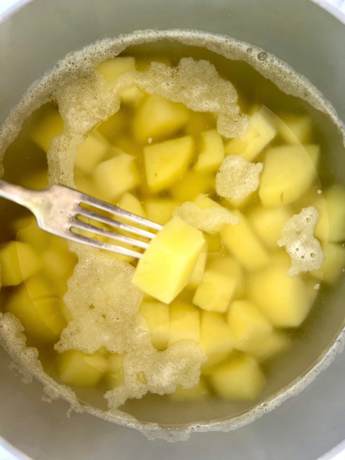 A fork checking diced potatoes for doneness.