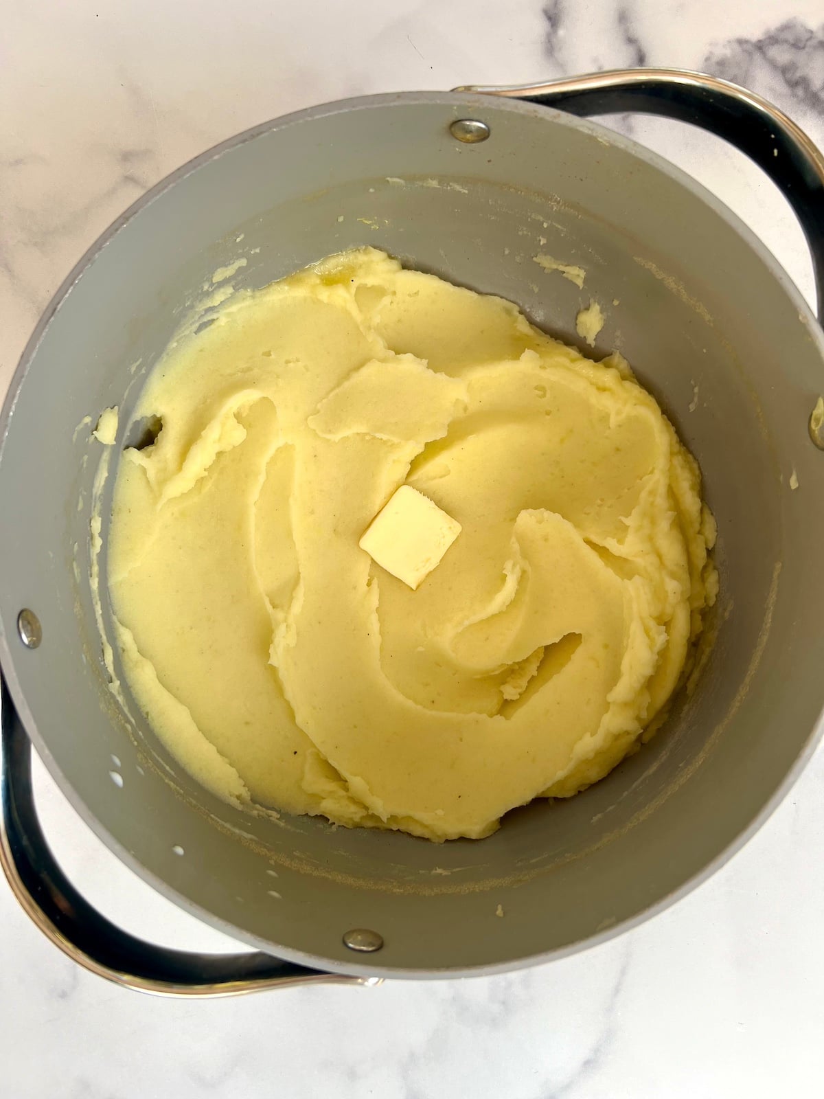 A pat of butter over a bowl of mashed potatoes.