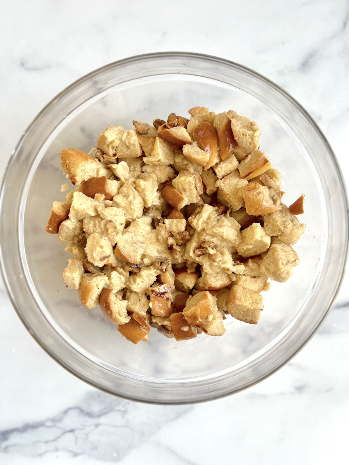Custard over cubed bread in a mixing bowl.