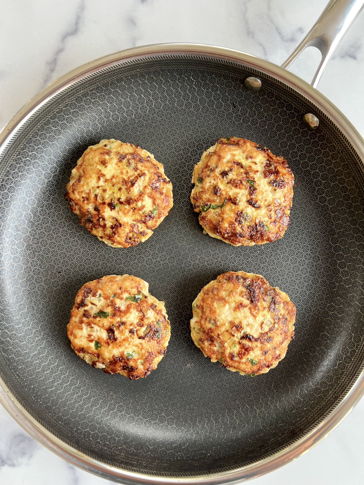 Middle eastern chicken burgers cooked in a sauté pan.
