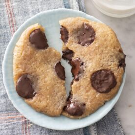 Microwave chocolate chip cookie broken in half on a plate.