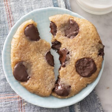Microwave chocolate chip cookie broken in half on a plate.