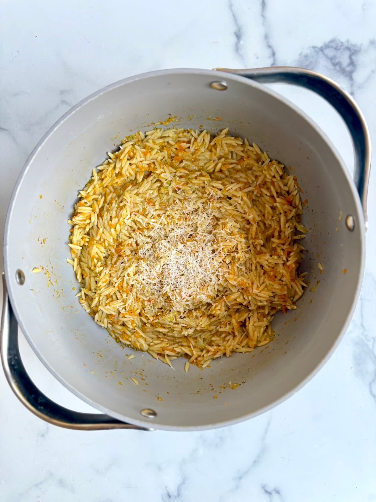 Carrot broccoli and cheese orzo in stock pot.