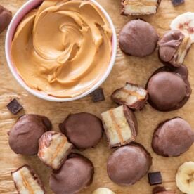 Banana chocolate peanut butter bites on a sheet tray with a bowl of peanut butter beside them.