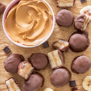 Banana chocolate peanut butter bites on a sheet tray with a bowl of peanut butter beside them.