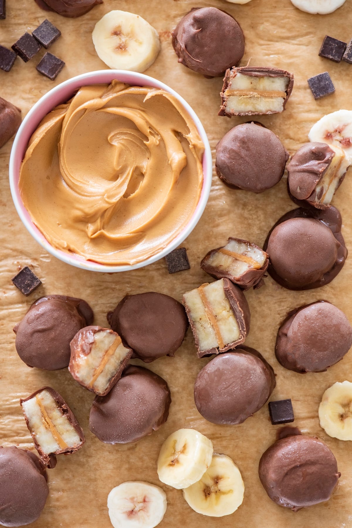 Banana chocolate peanut butter bites on a sheet tray with a bowl of peanut butter beside them.