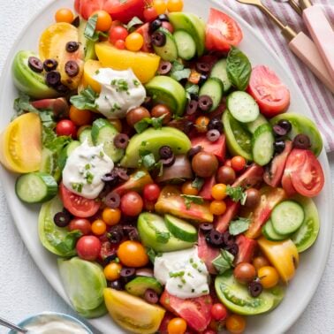 Heirloom tomato salad topped with Greek yogurt dressing on a big serving platter.