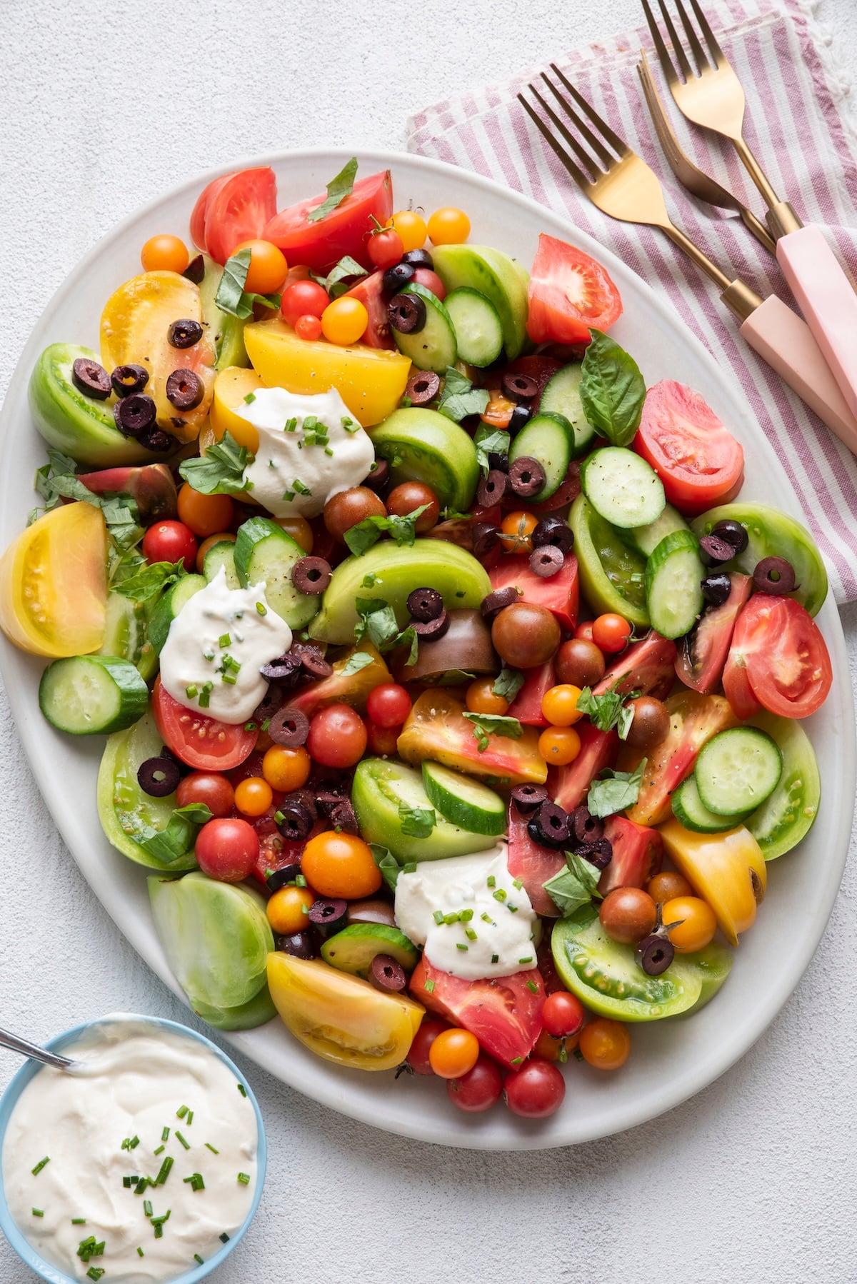 Heirloom tomato salad topped with Greek yogurt dressing on a big serving platter.