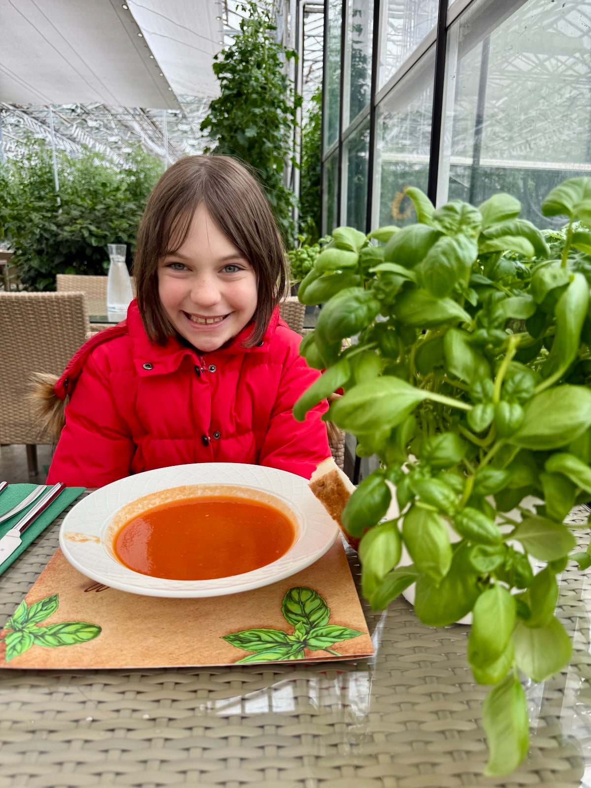 Young girl smiles with a bowl of tomato soup in front of her.