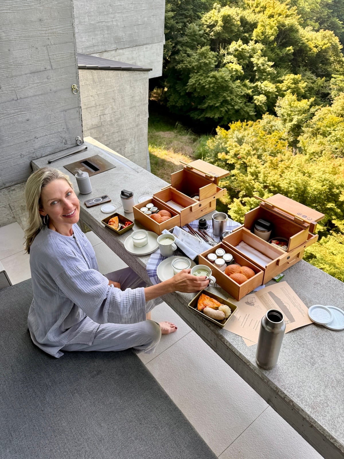 Woman with bento box style breakfast on balcony overlooking forest.