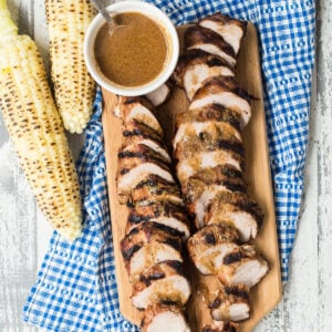 Southern style pork tenderloin sliced on a cutting board and served with grilled corn.