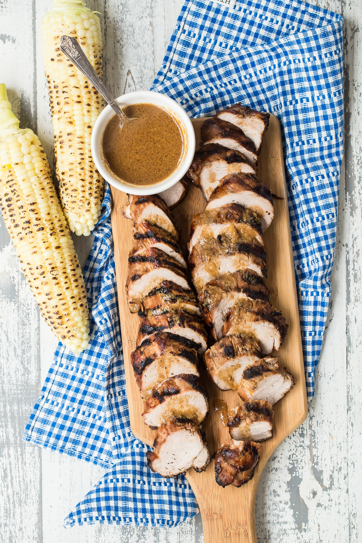 Southern style pork tenderloin sliced on a cutting board and served with grilled corn.