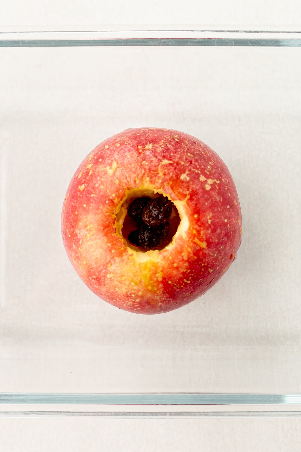 Cored apple filled with raisins in a baking dish.