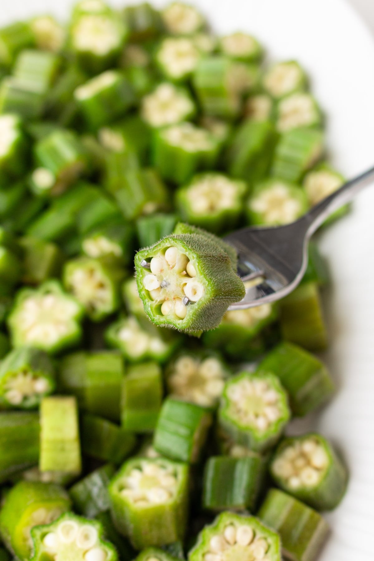 A fork holding a piece of okra over a plate of okra.
