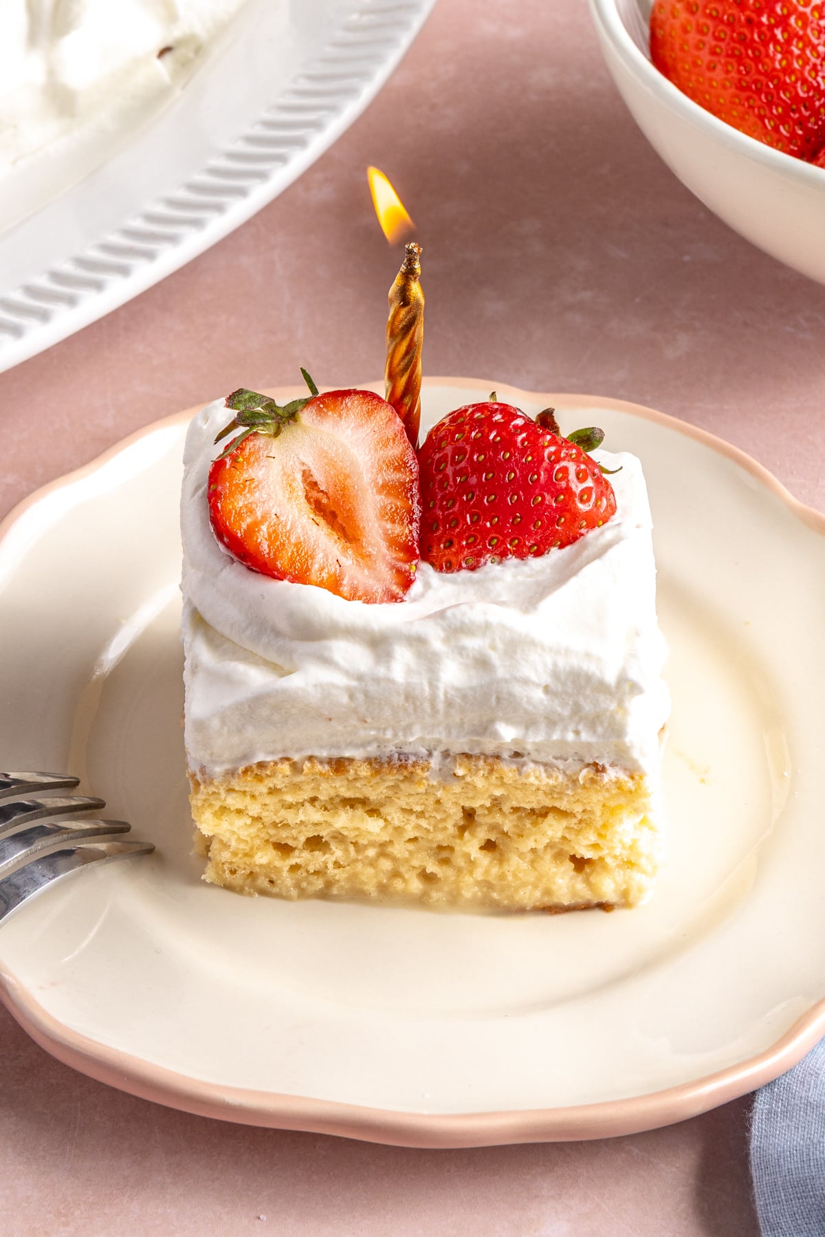 Piece of tres leches cake with a birthday candle on top.
