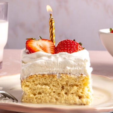 A slice of tres leches cake with a birthday candle on top.