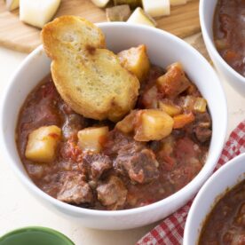 A bowl of beef stew with a piece of bread.
