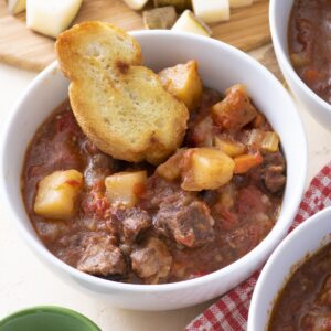 A bowl of beef stew with a piece of bread.
