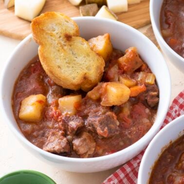 A bowl of beef stew with a piece of bread.