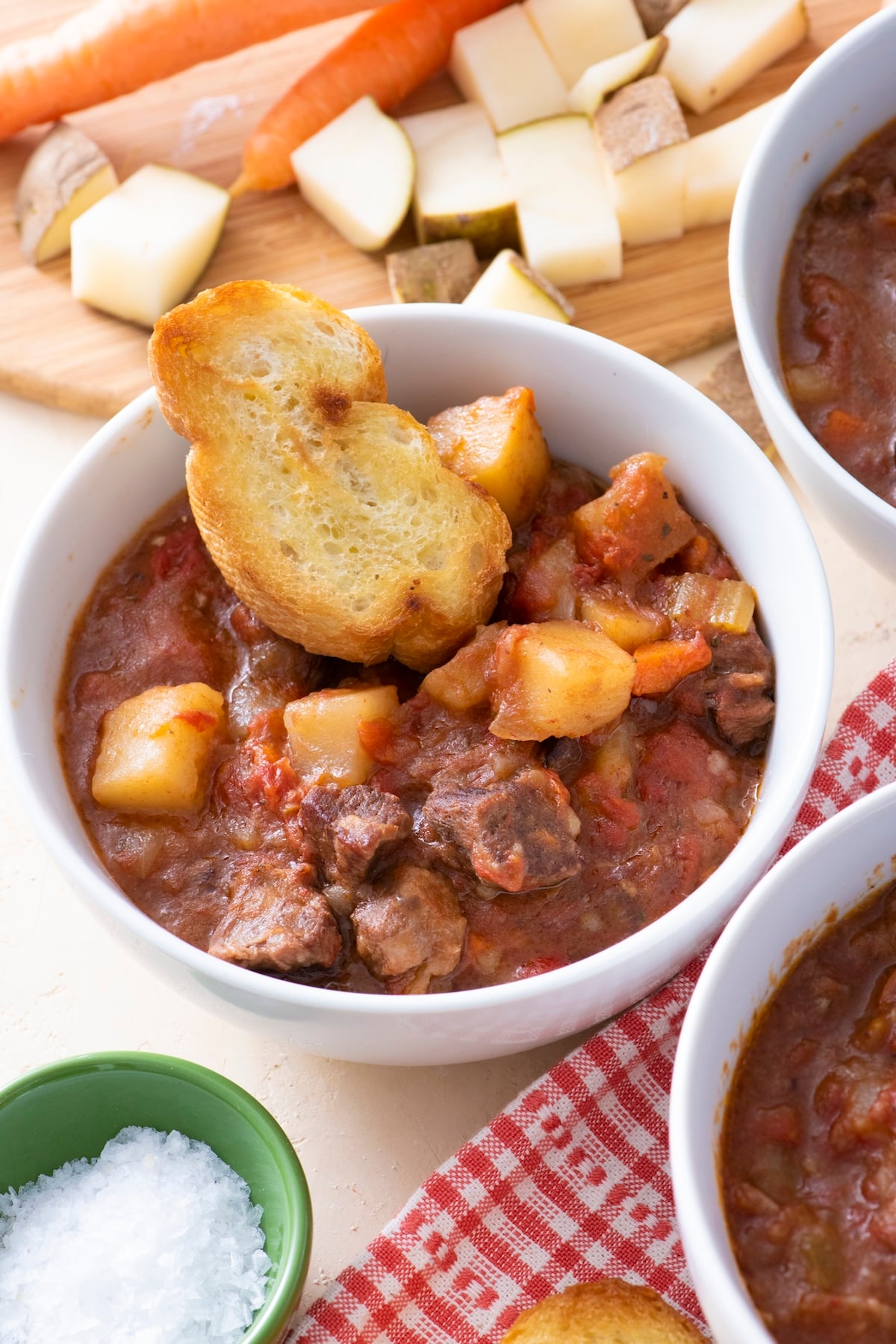 A bowl of beef stew with a piece of bread.