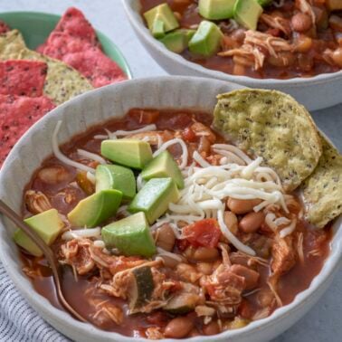 Slow cooker chicken chili in a bowl topped with avocado chunks.
